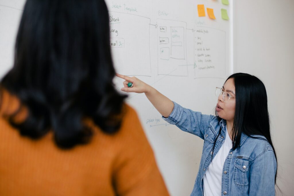 Female person pointing at white board and speaking.