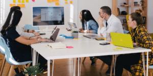 Group of people sitting around a table looking at a screen.