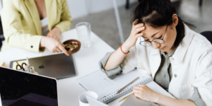 Two persons sitting at a table, one writing in an notebook, the other handing a bowl with pins